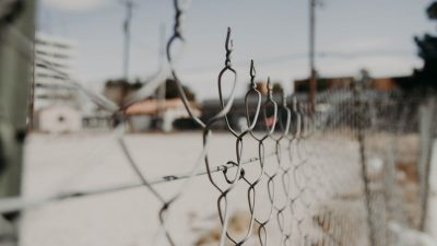 close up photo of chain link fence with out of focus buildings in the background