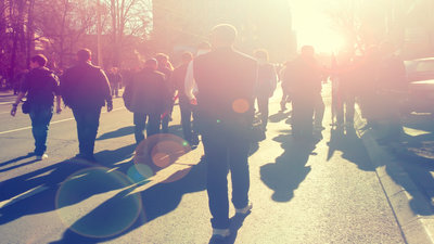 people walking down the street. a low sun shining in their direction