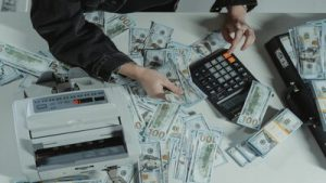 hand using calculator on table with U.S. currency scattered on it